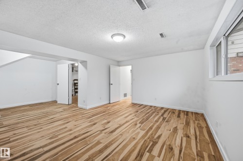 Spacious room featuring distinctive wood-finish flooring, white walls, and a large window - 13903 87 Street, Edmonton, AB - Indoor Photo Showing Other Room