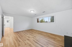 Spacious room featuring light wood-finish flooring, white painted walls, and a large horizontal window providing natural illumination - 