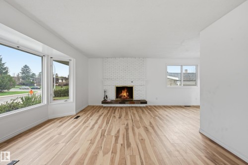 Living area featuring wood-finish flooring, a white brick fireplace with a dark-toned hearth, and expansive bay windows - 13903 87 Street, Edmonton, AB - Indoor Photo Showing Living Room With Fireplace