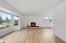 Living area featuring wood-finish flooring, a white brick fireplace with a dark-toned hearth, and expansive bay windows - 13903 87 Street, Edmonton, AB  - Indoor Photo Showing Living Room With Fireplace 