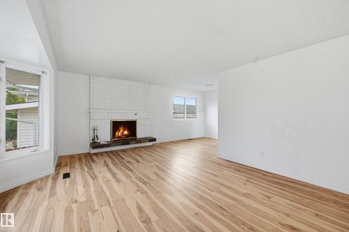 Spacious interior with wood-finish flooring, a white-painted brick fireplace with a dark stone hearth, and a bay window featuring white trim - 13903 87 Street, Edmonton, AB - Indoor Photo Showing Living Room With Fireplace