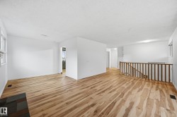 Spacious open-concept living area featuring wood-finish flooring, crisp white walls, and abundant natural light from multiple windows - 