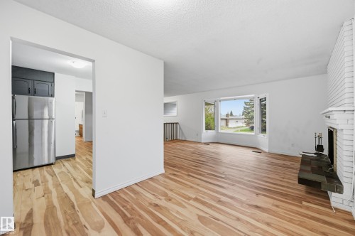 Bright living area featuring wood-finish flooring, a white brick fireplace with hearth, and a large bay window - 13903 87 Street, Edmonton, AB - Indoor With Fireplace