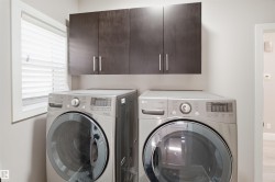 Laundry area featuring a side-by-side washer and dryer, dark wood-finish cabinetry with silver hardware, and a window with white blinds - 