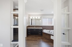 Well-appointed bathroom featuring a corner soaking tub, a double vanity with stone countertop, wood-finish tile flooring, and a separate shower enclosure - 