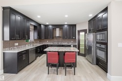 Kitchen featuring dark wood cabinetry, light wood-finish flooring, recessed lighting, stainless steel appliances, and a central island with a stone countertop - 