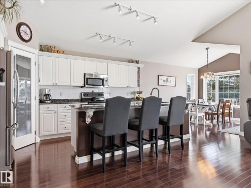 Open-concept kitchen featuring white cabinetry, stainless steel appliances, dark wood-finish flooring, and a central island with countertop seating - 1340 Oakland Crescent, Devon, AB - Indoor