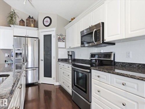 Kitchen featuring white cabinetry, stainless steel appliances, dark granite countertops, and wood-finish flooring - 1340 Oakland Crescent, Devon, AB - Indoor Photo Showing Kitchen With Upgraded Kitchen