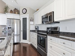 Kitchen featuring white cabinetry, stainless steel appliances, dark granite countertops, and wood-finish flooring - 