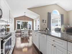 Kitchen featuring an expansive island with a built-in sink, white cabinetry, and dark countertop surfaces - 