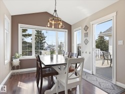 Dining area featuring a vaulted ceiling, wood-finish flooring, a contemporary chandelier, large windows with grid patterns, and direct access to an outdoor deck - 