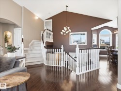 Hardwood-finish flooring extending through the main level, complemented by a grand staircase with white balusters and dark wood handrails - 