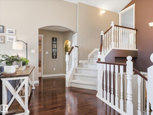 Two-story staircase with white balusters and dark wood handrails, hardwood flooring, arched doorway, and recessed wall niche - 1340 Oakland Crescent, Devon, AB - Indoor Photo Showing Other Room