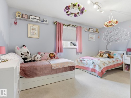 Light gray painted walls with a decorative tree decal, plush carpeting, and two windows with roller shades - 1340 Oakland Crescent, Devon, AB - Indoor Photo Showing Bedroom