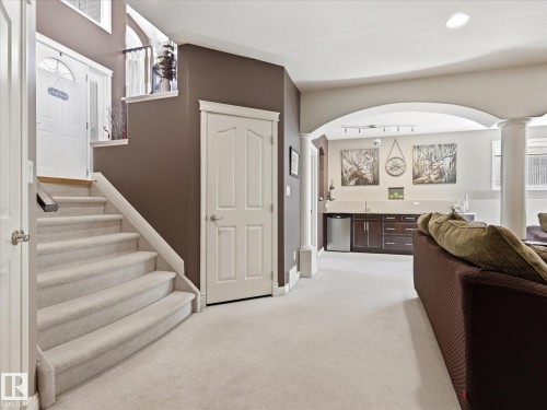 Carpeted staircase with white balustrade leading to a main entrance door with a transom window - 1340 Oakland Crescent, Devon, AB - Indoor Photo Showing Other Room