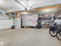 Spacious garage featuring a concrete floor, built-in overhead shelving, a utility door, an integrated workbench, and a pegboard tool organization system - 