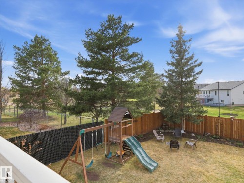 Expansive backyard featuring a wooden privacy fence, mature trees, and a play structure - 1340 Oakland Crescent, Devon, AB - Outdoor With Backyard