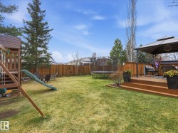 Expansive backyard featuring a multi-level wood deck with a gazebo, established green lawn, tall privacy fencing, and mature trees - 