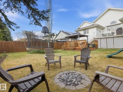 Expansive backyard featuring a stone-ringed fire pit, wood privacy fencing, a multi-level wood deck with a gazebo, and a secondary white deck with railings - 