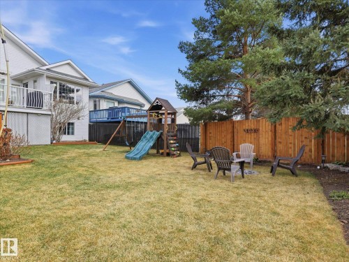 Spacious backyard featuring a manicured lawn, a wooden privacy fence, and mature evergreen trees - 1340 Oakland Crescent, Devon, AB - Outdoor With Deck Patio Veranda