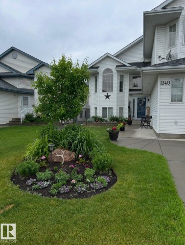 White siding exterior with a prominent arched window, established front landscaping, a paved walkway, and a manicured lawn - 1340 Oakland Crescent, Devon, AB - Outdoor With Facade