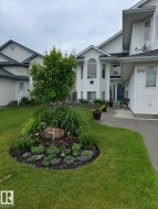 White siding exterior with a prominent arched window, established front landscaping, a paved walkway, and a manicured lawn - 