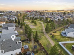 Aerial perspective showcasing a residential neighborhood with a central park featuring a paved walking path, mature trees, and open green spaces - 