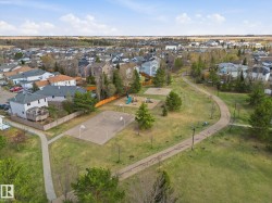 Expansive green space featuring a playground, basketball court, paved walking paths, and mature trees - 