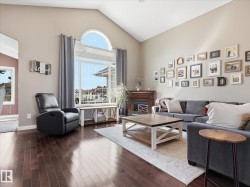 Spacious living area featuring high vaulted ceilings, rich wood-finish flooring, and a prominent fireplace with a wood mantel - 