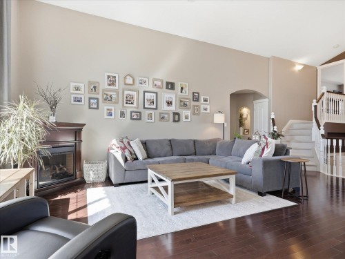 Spacious living area featuring wood-finish flooring, a traditional fireplace with a dark wood mantel, and an arched entryway - 1340 Oakland Crescent, Devon, AB - Indoor Photo Showing Living Room