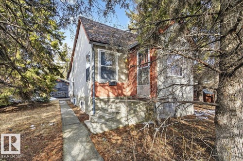 The property features exterior stucco and brick finishes, a concrete pathway, and mature trees surrounding the home - 12942 68 Street, Edmonton, AB 