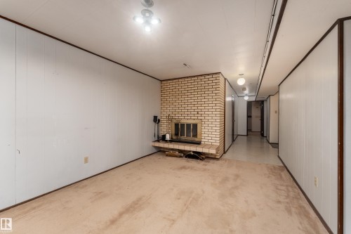 Living area featuring a brick fireplace with a raised hearth, light-toned carpeting, white paneling, and a hallway with light-colored flooring - 3711 118 Street, Edmonton, AB - Indoor Photo Showing Other Room