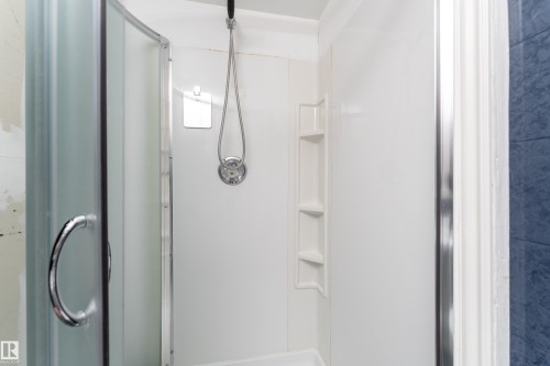Shower enclosure featuring a curved glass door with chrome hardware, white paneling, integrated shelving, and a handheld showerhead with a chrome fixture - 3711 118 Street, Edmonton, AB - Indoor Photo Showing Bathroom