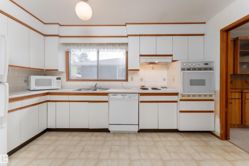 Kitchen featuring extensive white cabinetry with wood-finish trim, a built-in wall oven, and a tiled backsplash - 3711 118 Street, Edmonton, AB - Indoor Photo Showing Kitchen With Double Sink