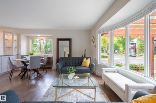 Bright living area featuring expansive bay windows with white trim, wood-finish flooring, and built-in cabinetry with glass display doors - 14604 92A Avenue, Edmonton, AB - Indoor Photo Showing Living Room
