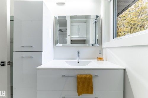 White vanity with an integrated sink and chrome faucet, framed mirror, and a tall storage cabinet with horizontal pulls - 14604 92A Avenue, Edmonton, AB - Indoor Photo Showing Bathroom