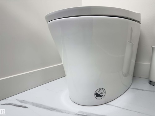 Modern white toilet with integrated bidet functionality, set against a white wall with crisp baseboards, and complemented by marble-finish floor tiling - 14604 92A Avenue, Edmonton, AB - Indoor