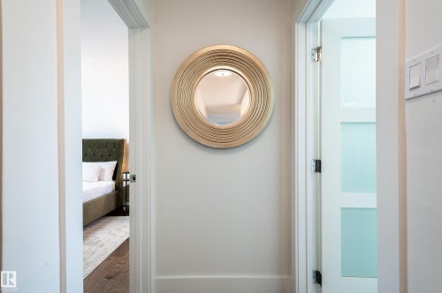 Hallway featuring a decorative round mirror with a textured gold-tone frame, white baseboards, and light-colored wall paint - 14604 92A Avenue, Edmonton, AB - Indoor Photo Showing Other Room