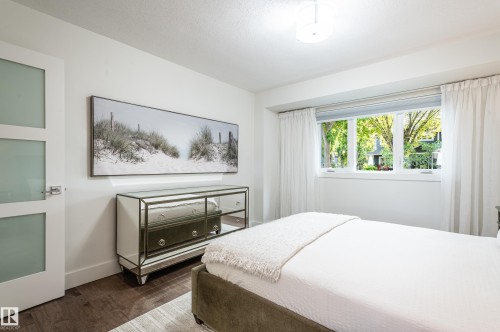 Bright bedroom featuring a large window with exterior greenery, wood-finish flooring, white walls, and a contemporary flush-mount ceiling light - 14604 92A Avenue, Edmonton, AB - Indoor Photo Showing Bedroom