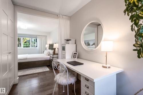 Dedicated workspace featuring a white desk with built-in drawers, wood-finish flooring, and a contemporary wall mirror - 14604 92A Avenue, Edmonton, AB - Indoor