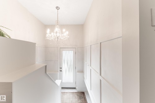 Bright entryway featuring a crystal chandelier, board and batten wall detailing, a decorative glass door, and a staircase with a half-wall railing - 14604 92A Avenue, Edmonton, AB - Indoor Photo Showing Other Room