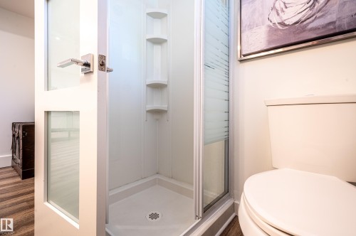 Three-piece bathroom featuring a corner shower with integrated shelving, a white toilet, and wood-finish flooring - 14604 92A Avenue, Edmonton, AB - Indoor Photo Showing Bathroom