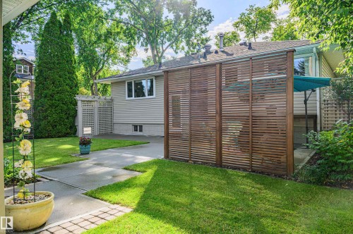 Manicured backyard featuring a contemporary slatted wood privacy screen, mature trees, and a concrete patio space - 14604 92A Avenue, Edmonton, AB - Outdoor