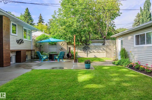 Spacious backyard featuring a concrete patio, verdant lawn, mature trees, and a decorative lattice privacy screen - 14604 92A Avenue, Edmonton, AB - Outdoor