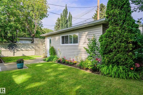 Manicured backyard featuring a light-colored privacy fence with decorative lattice, a paved pathway, and a detached building with horizontal siding - 14604 92A Avenue, Edmonton, AB - Outdoor
