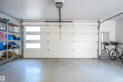 Spacious garage featuring a modern sectional overhead door with frosted glass panels, an automatic opener, and a durable epoxy-coated concrete floor - 14604 92A Avenue, Edmonton, AB - Indoor Photo Showing Garage