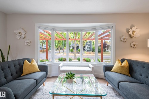 Bright living area featuring a large bay window with white trim, light-colored walls, and wood-finish flooring - 14604 92A Avenue, Edmonton, AB - Indoor Photo Showing Living Room