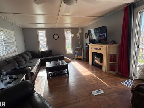 Living area featuring wood-finish flooring, light gray walls, multiple windows with blinds, a built-in electric fireplace, and a ceiling fan. - 115 2Nd Street E, Derwent, AB - Indoor Photo Showing Living Room With Fireplace
