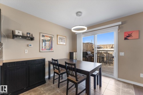 Dining area featuring tile flooring, a contemporary pendant light fixture, a built-in black cabinet with a wood-finish countertop, and sliding glass doors opening to an outdoor deck - 21818 99A Avenue, Edmonton, AB - Indoor Photo Showing Dining Room