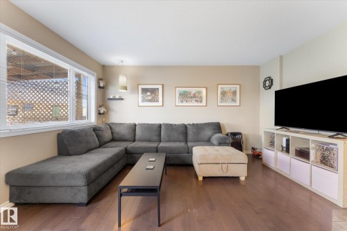 Living area featuring wood-finish flooring, neutral wall tones, and a large window with white blinds - 21818 99A Avenue, Edmonton, AB - Indoor Photo Showing Living Room